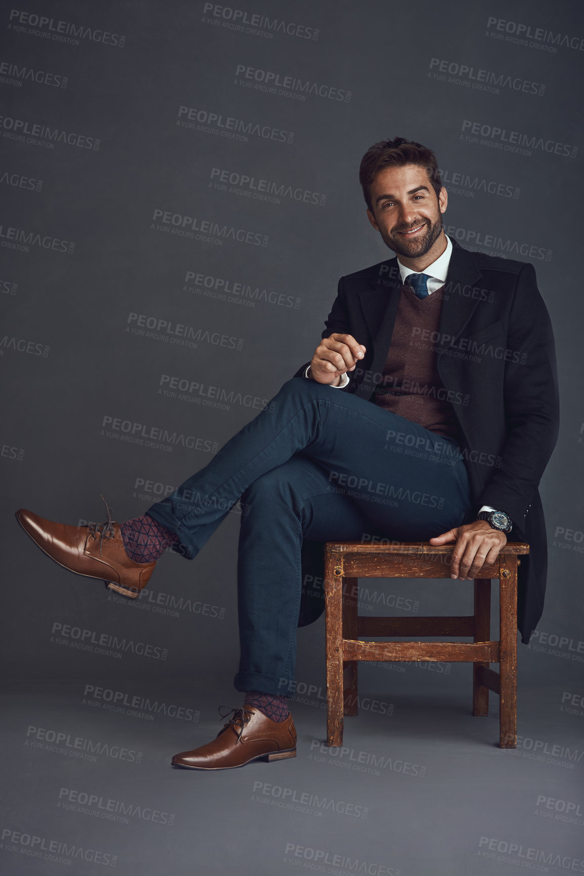 Buy stock photo Studio portrait of a stylishly dressed young man sitting on a chair against a gray background