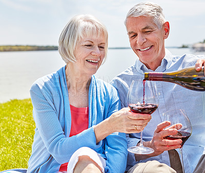 Buy stock photo Shot of a happy senior couple having a picnic together outside and enjoying some wine