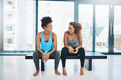 Buy stock photo Portrait shot of two young fit women sitting down on a bench and having a chat before a yoga session inside a studio