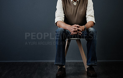 Buy stock photo Studio shot of an unrecognizable man sitting on a wooden stool against a dark background