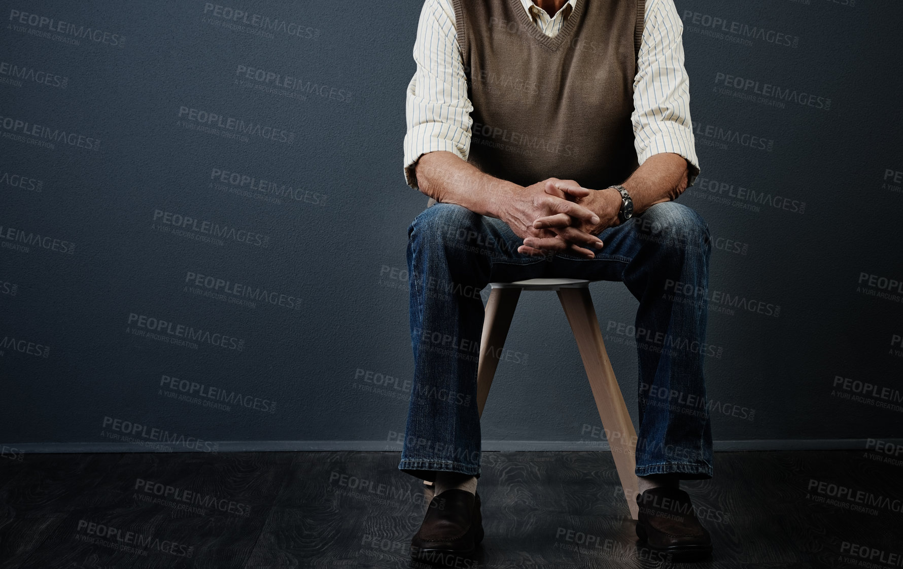 Buy stock photo Studio shot of an unrecognizable man sitting on a wooden stool against a dark background