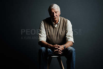 Buy stock photo Studio shot of a handsome mature man looking thoughtful while sitting on a stool against a dark background