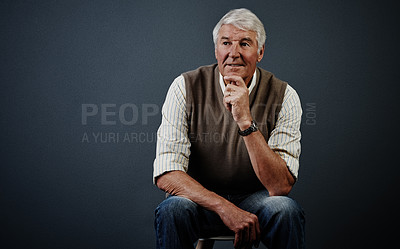 Buy stock photo Studio shot of a handsome mature man looking thoughtful while sitting on a stool against a dark background