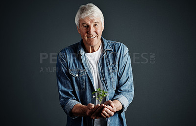 Buy stock photo Studio portrait of a handsome mature man holding a budding plant against a dark background