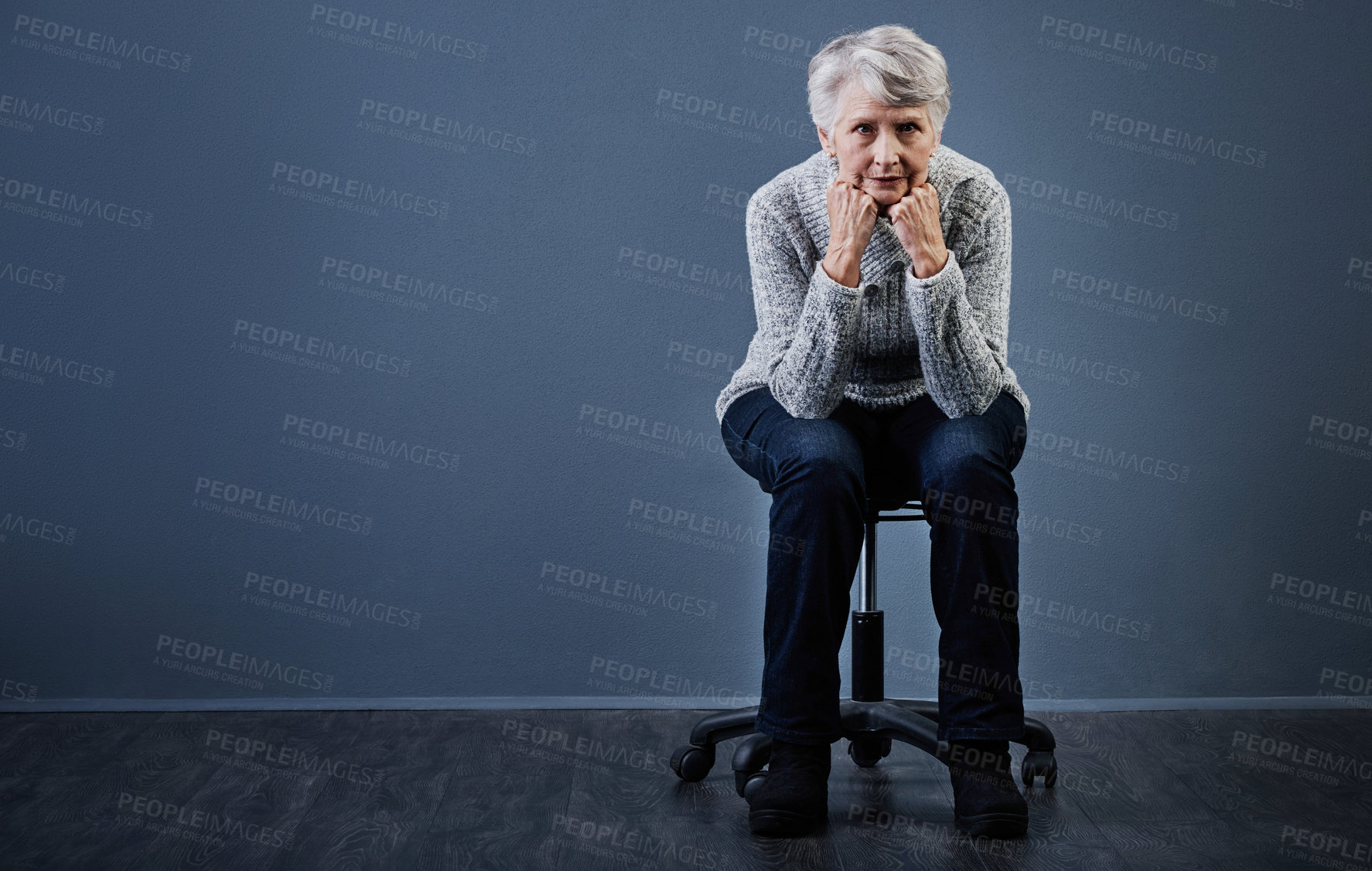 Buy stock photo Studio shot of an elderly woman sitting with her hands under her chin while looking at the camera