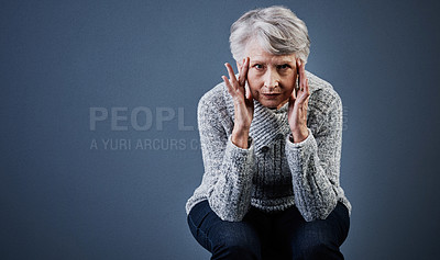 Buy stock photo Studio shot of a elderly woman sitting with her hands touching the sides of her head while looking at the camera