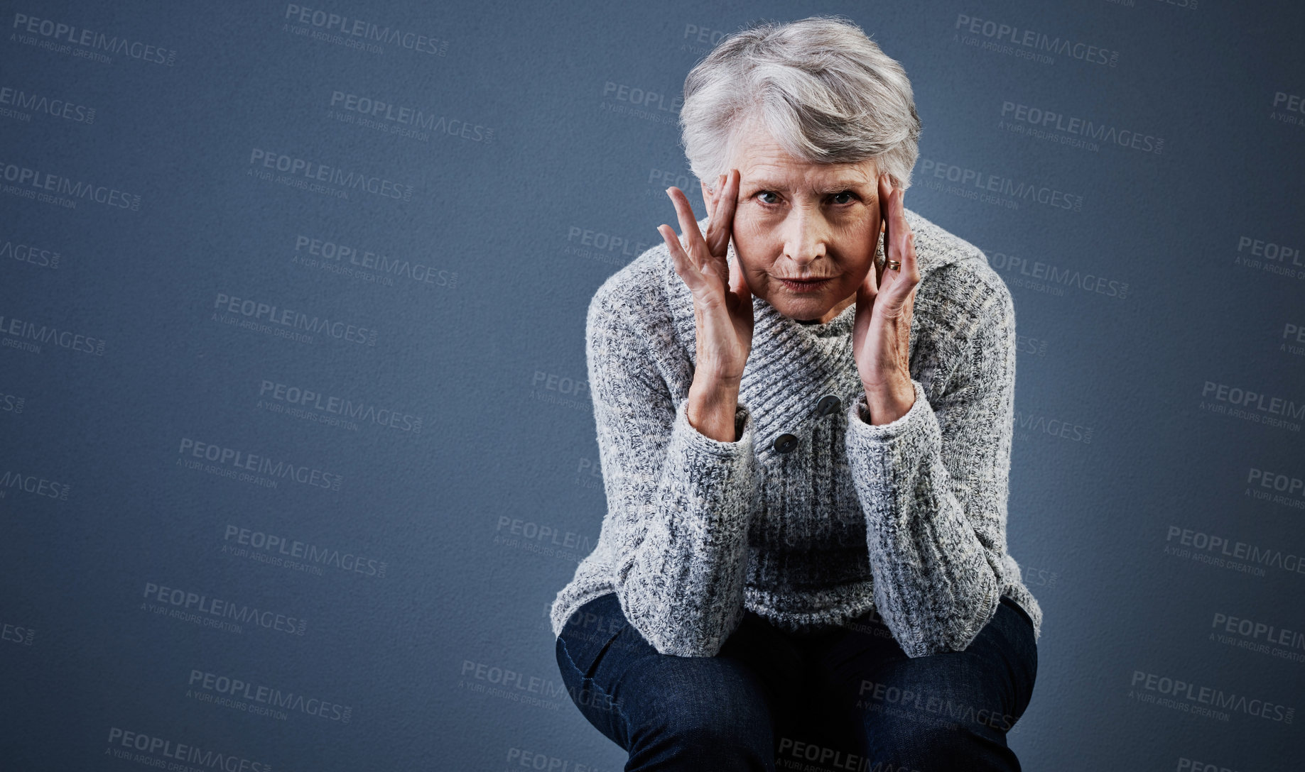 Buy stock photo Studio shot of a elderly woman sitting with her hands touching the sides of her head while looking at the camera