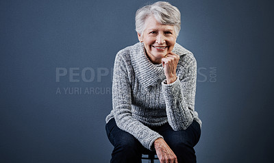 Buy stock photo Studio shot of a cheerful elderly woman sitting with her one hand under her chin and posing while looking at the camera