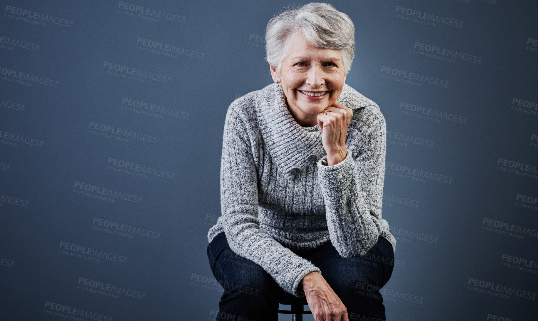 Buy stock photo Studio shot of a cheerful elderly woman sitting with her one hand under her chin and posing while looking at the camera