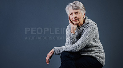 Buy stock photo Studio shot a confident elderly woman sitting down and touching the side of her face while looking into the distance