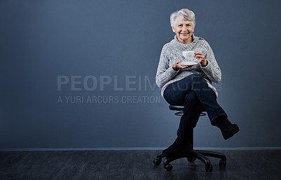 Buy stock photo Studio shot of a cheerful elderly woman sitting down and enjoying a cup of tea while looking at the camera