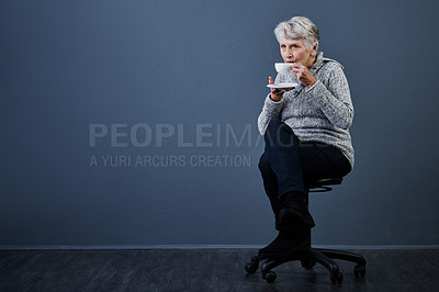 Buy stock photo Studio shot of an elderly woman sitting down and enjoying a cup of tea on her own