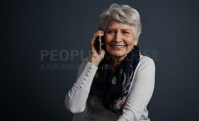 Buy stock photo Studio shot of a cheerful elderly woman sitting down and talking on her cellphone