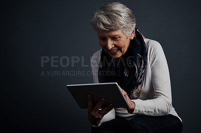 Buy stock photo Studio shot of an cheerful elderly woman standing and using a tablet