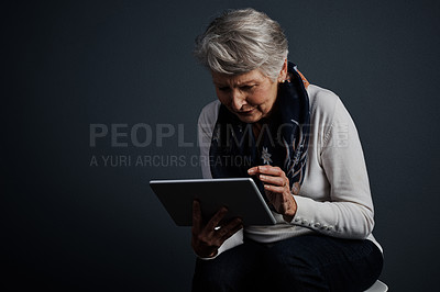 Buy stock photo Studio shot of an  elderly woman sitting and using a tablet