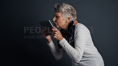 Buy stock photo Studio shot of a cheerful elderly woman standing and giving her tablet a kiss