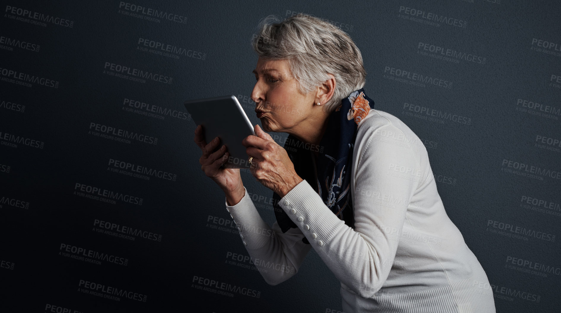 Buy stock photo Studio shot of a cheerful elderly woman standing and giving her tablet a kiss