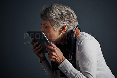 Buy stock photo Studio shot of a cheerful elderly woman standing and giving her tablet a kiss