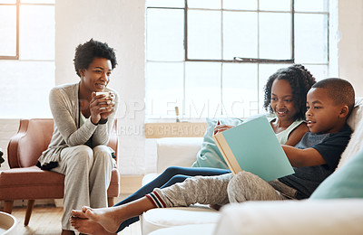 Buy stock photo Shot of a little brother and sister reading a book while their mother watches at home