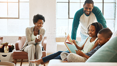 Buy stock photo Shot of a little brother and sister reading a book while their parents watch at home