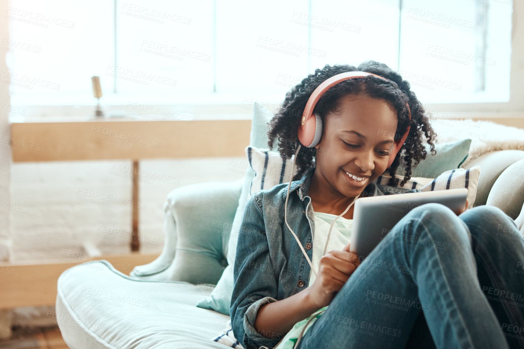 Buy stock photo Tablet, headphones and black girl on the sofa to relax while listening to music, radio or podcast. Rest, technology and African child watching a video on mobile device in her living room at home.