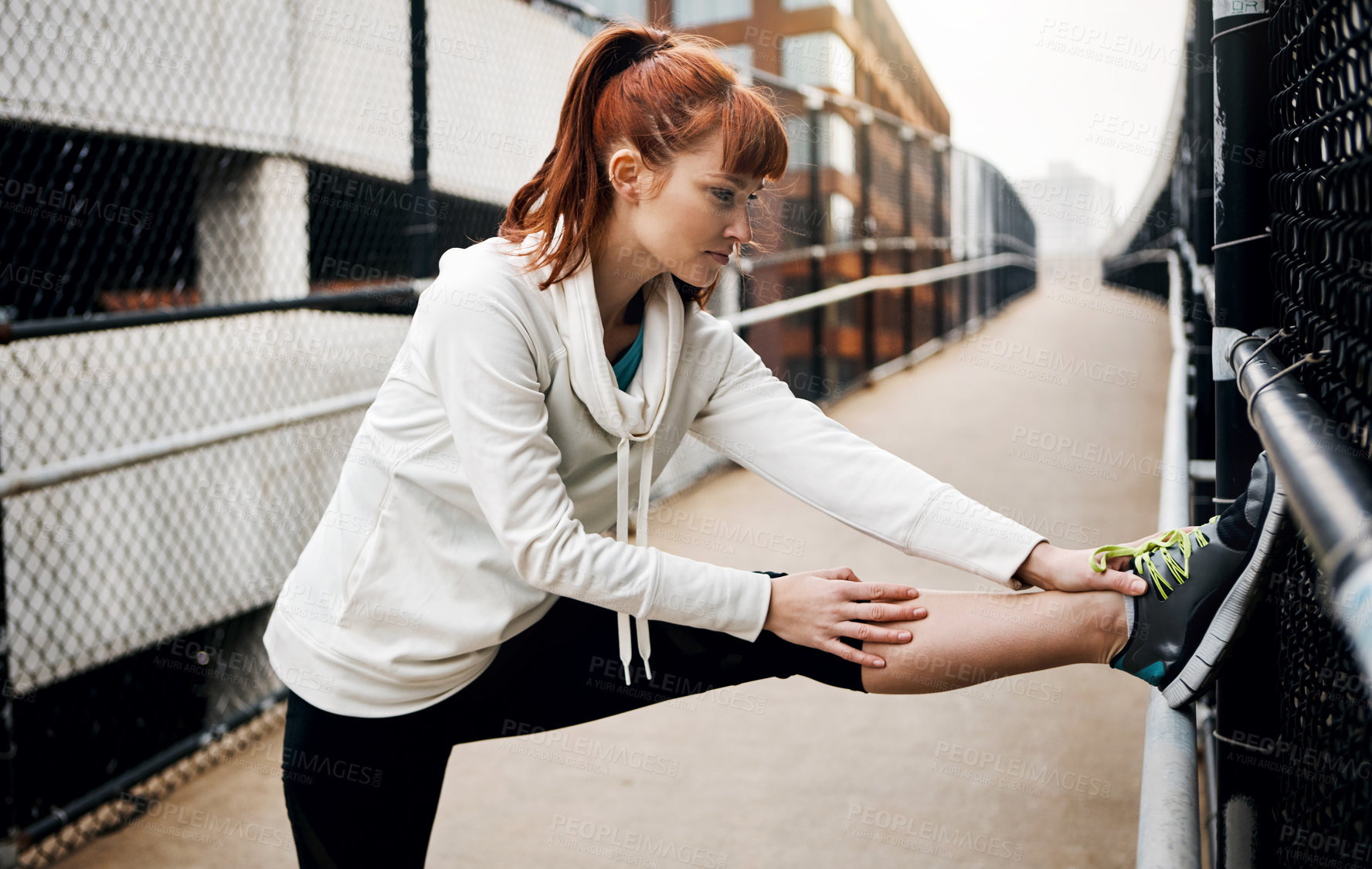 Buy stock photo Cropped shot of an attractive young woman stretching before her run in the city