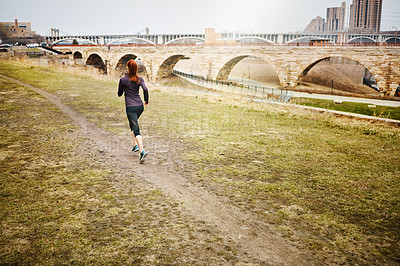 Buy stock photo Rear view shot of a sporty young woman running alongside the city