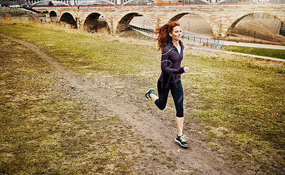 Buy stock photo Shot of a sporty young woman listening to music while running alongside the city