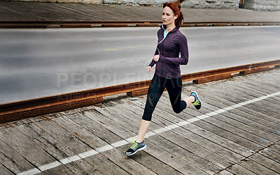 Buy stock photo Shot of a sporty young woman listening to music while running in the city