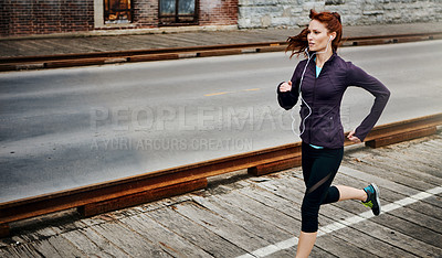 Buy stock photo Shot of a sporty young woman listening to music while running in the city