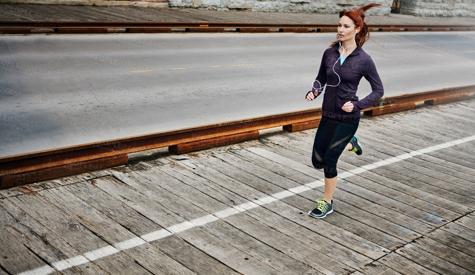 Buy stock photo Shot of a sporty young woman listening to music while running in the city