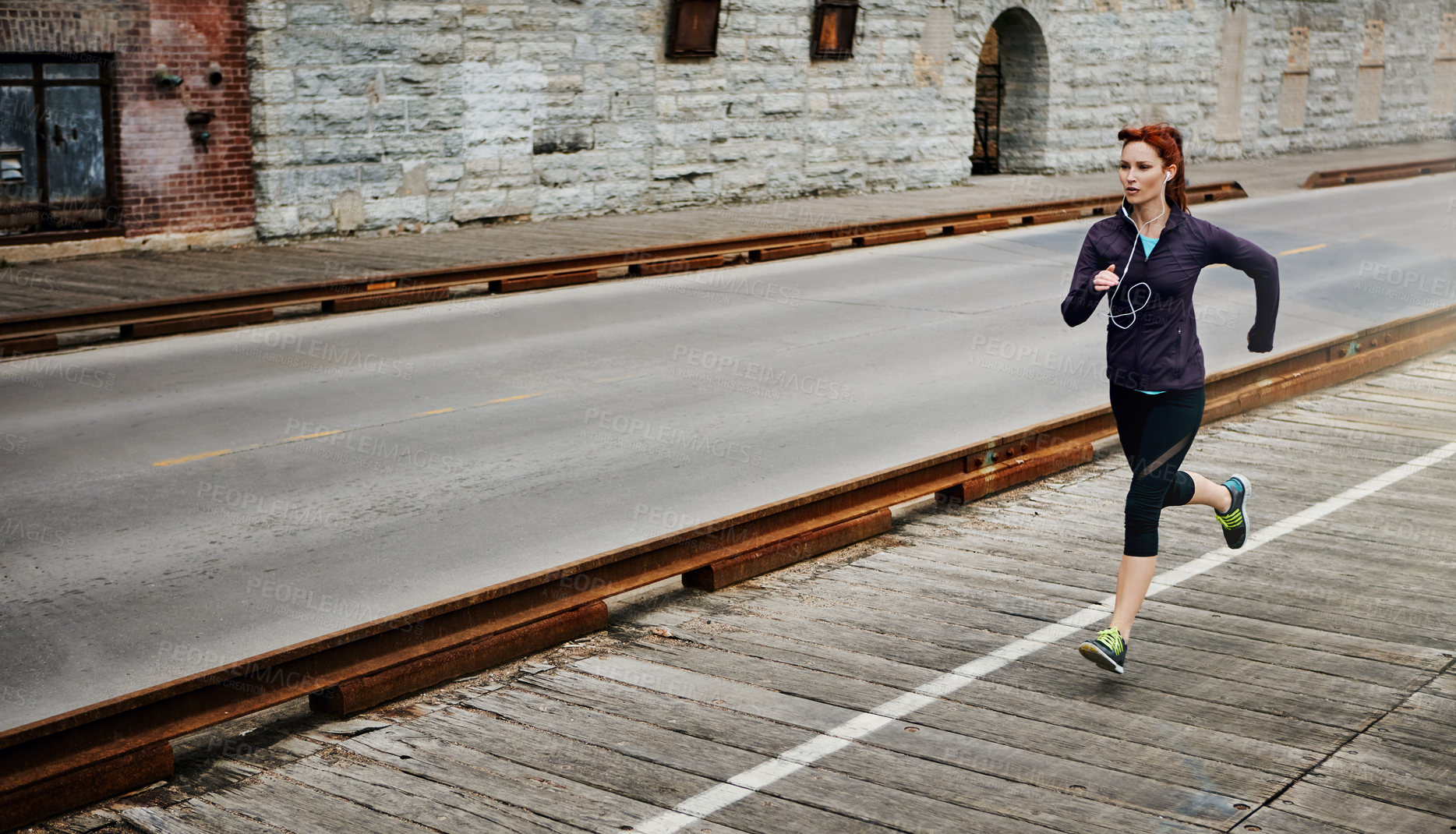 Buy stock photo Shot of a sporty young woman listening to music while running in the city