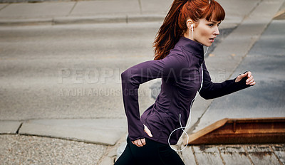 Buy stock photo Shot of a sporty young woman listening to music while running in the city