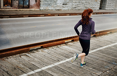 Buy stock photo Rear view shot of a sporty young woman listening to music while running in the city