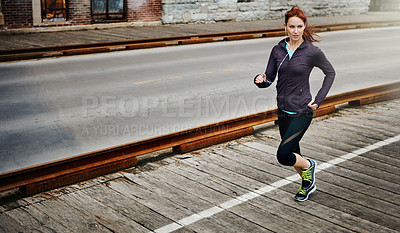 Buy stock photo Shot of a sporty young woman listening to music while running in the city