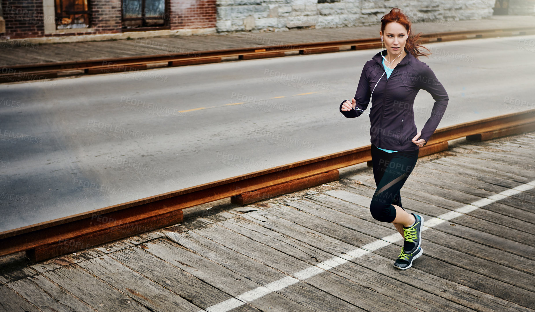 Buy stock photo Shot of a sporty young woman listening to music while running in the city