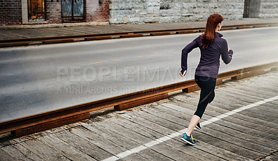 Buy stock photo Rear view shot of a sporty young woman listening to music while running in the city