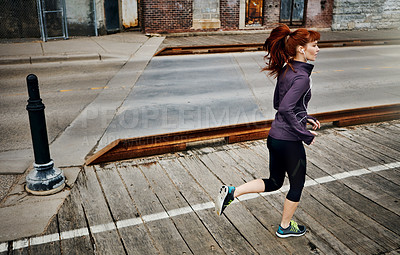 Buy stock photo Shot of a sporty young woman listening to music while running in the city