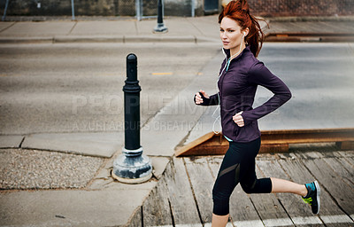 Buy stock photo Shot of a sporty young woman listening to music while running in the city