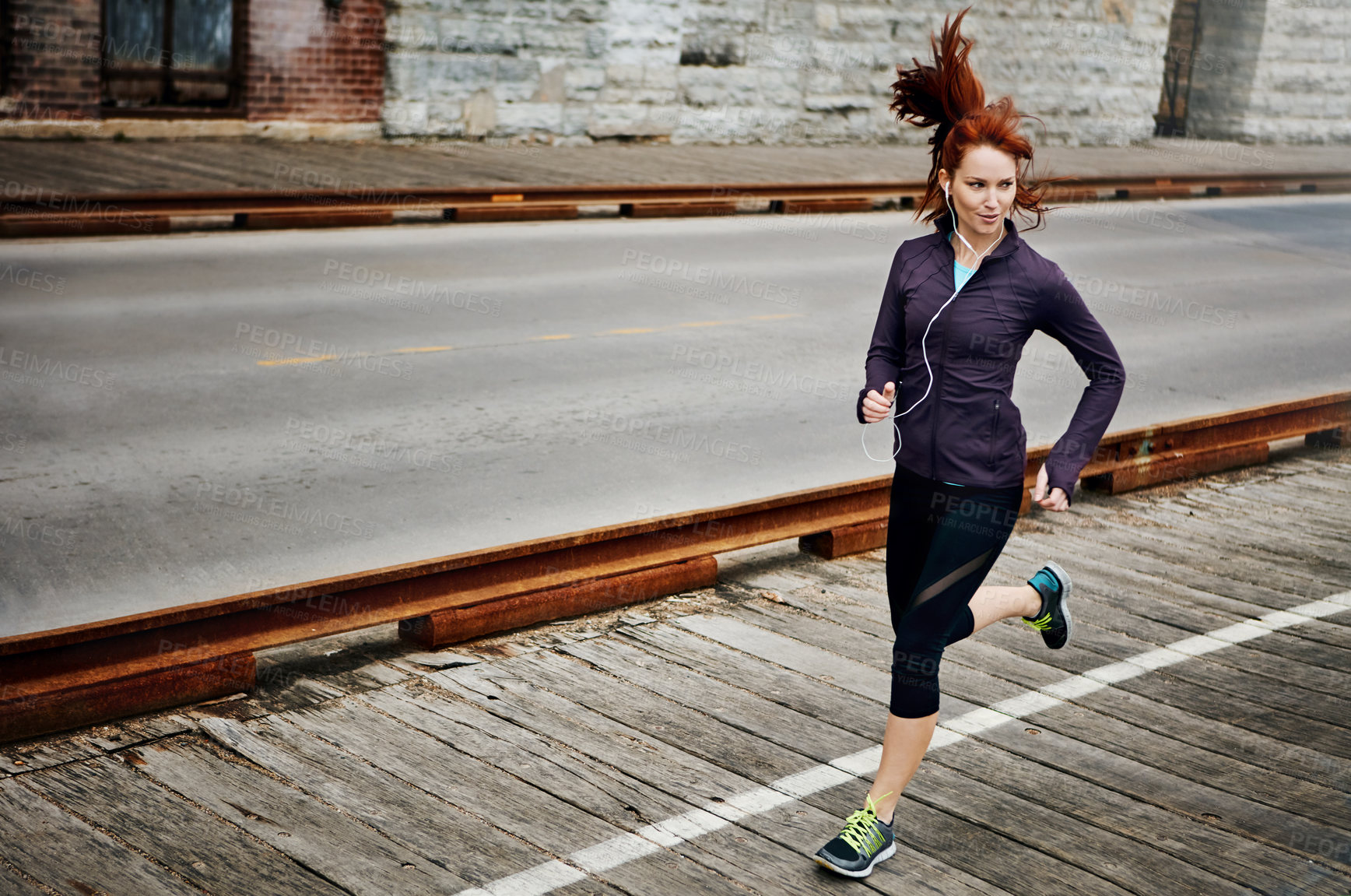 Buy stock photo Shot of a sporty young woman listening to music while running in the city