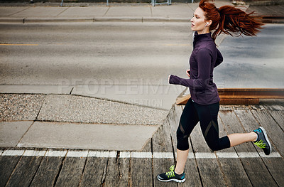 Buy stock photo Shot of a sporty young woman listening to music while running in the city