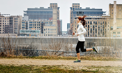 Buy stock photo Shot of a sporty young woman running alongside the city