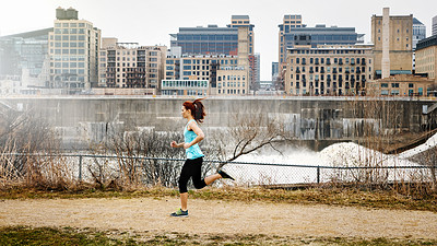 Buy stock photo Shot of a sporty young woman running alongside the city