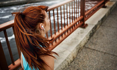 Buy stock photo Rear view shot of a sporty young woman listening to music while running in the city