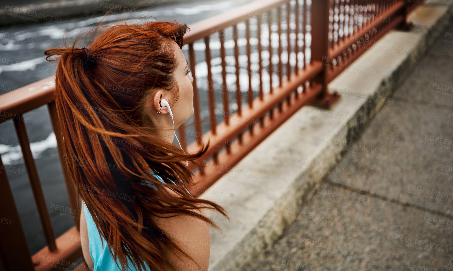 Buy stock photo Rear view shot of a sporty young woman listening to music while running in the city