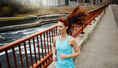 Buy stock photo Shot of a sporty young woman listening to music while running in the city