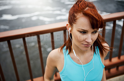 Buy stock photo Shot of a sporty young woman listening to music while out for a run in the city