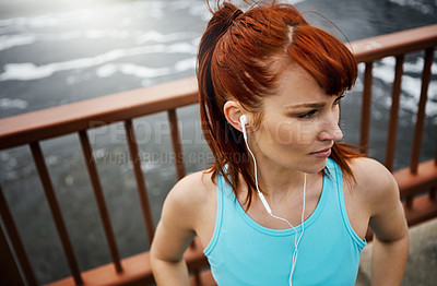 Buy stock photo Shot of a sporty young woman listening to music while out for a run in the city