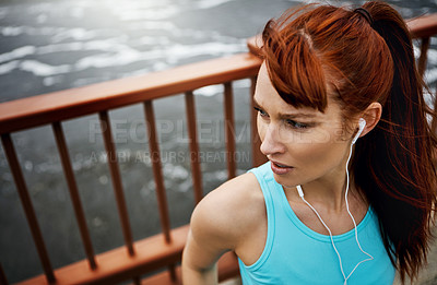 Buy stock photo Shot of a sporty young woman listening to music while out for a run in the city