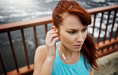 Buy stock photo Shot of a sporty young woman listening to music while out for a run in the city